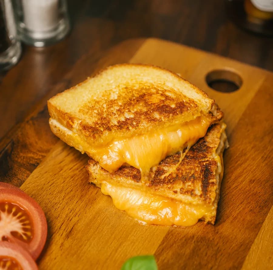 The Ultimate Cheese toastie cut in half on a wooden board, cheese pulling between the halves